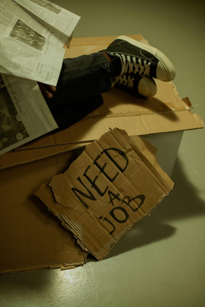 Image depicting a person reading a newspaper with a 'Need a Job' sign, highlighting unemployment issues.